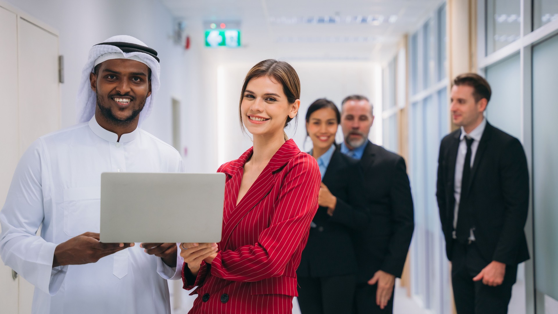 A group of different business people are sitting around a big meeting table in a modern office.